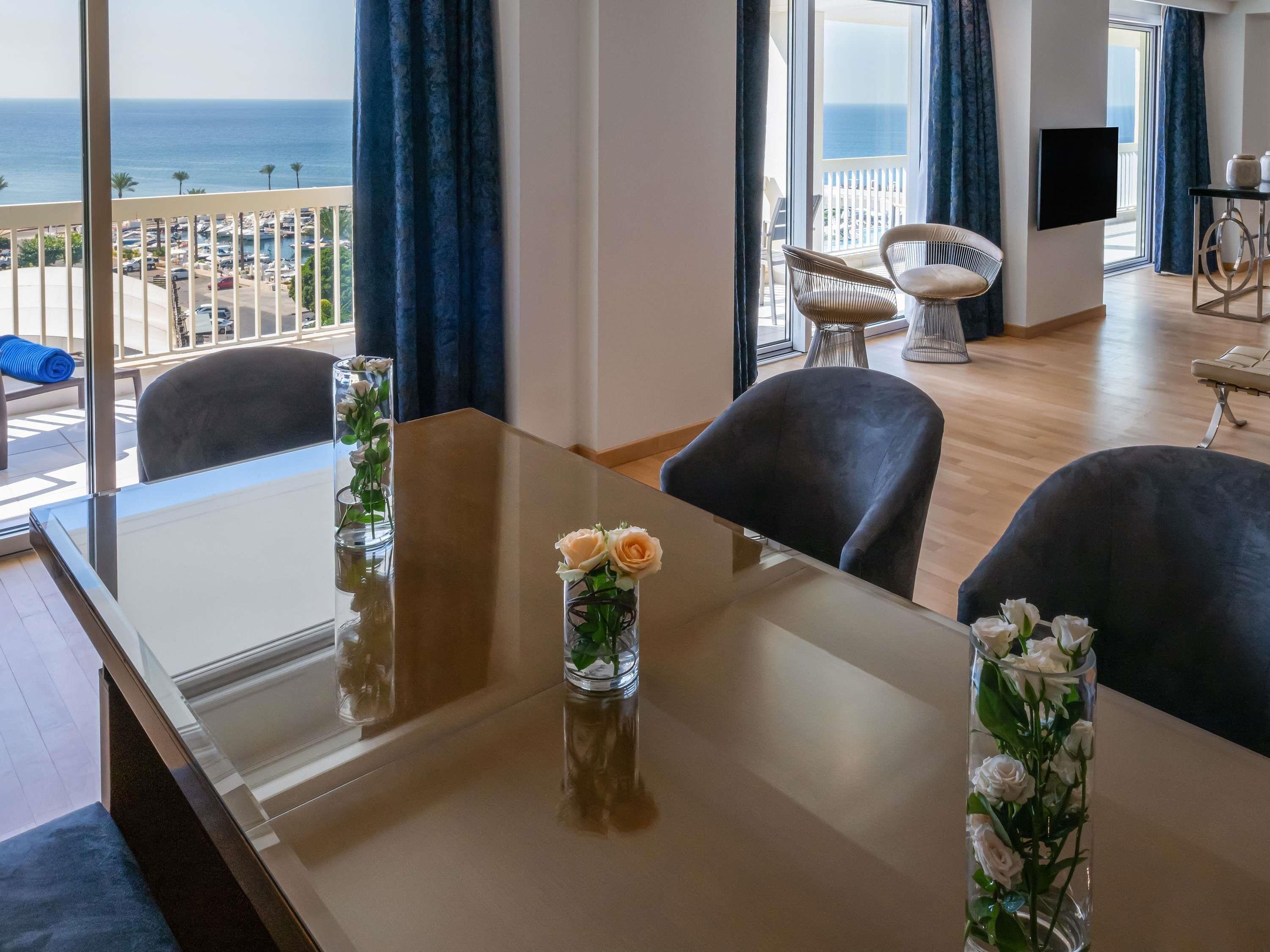Een moderne hotelkamer met balkon, een eettafel met stoelen en een aan de muur bevestigde televisie.