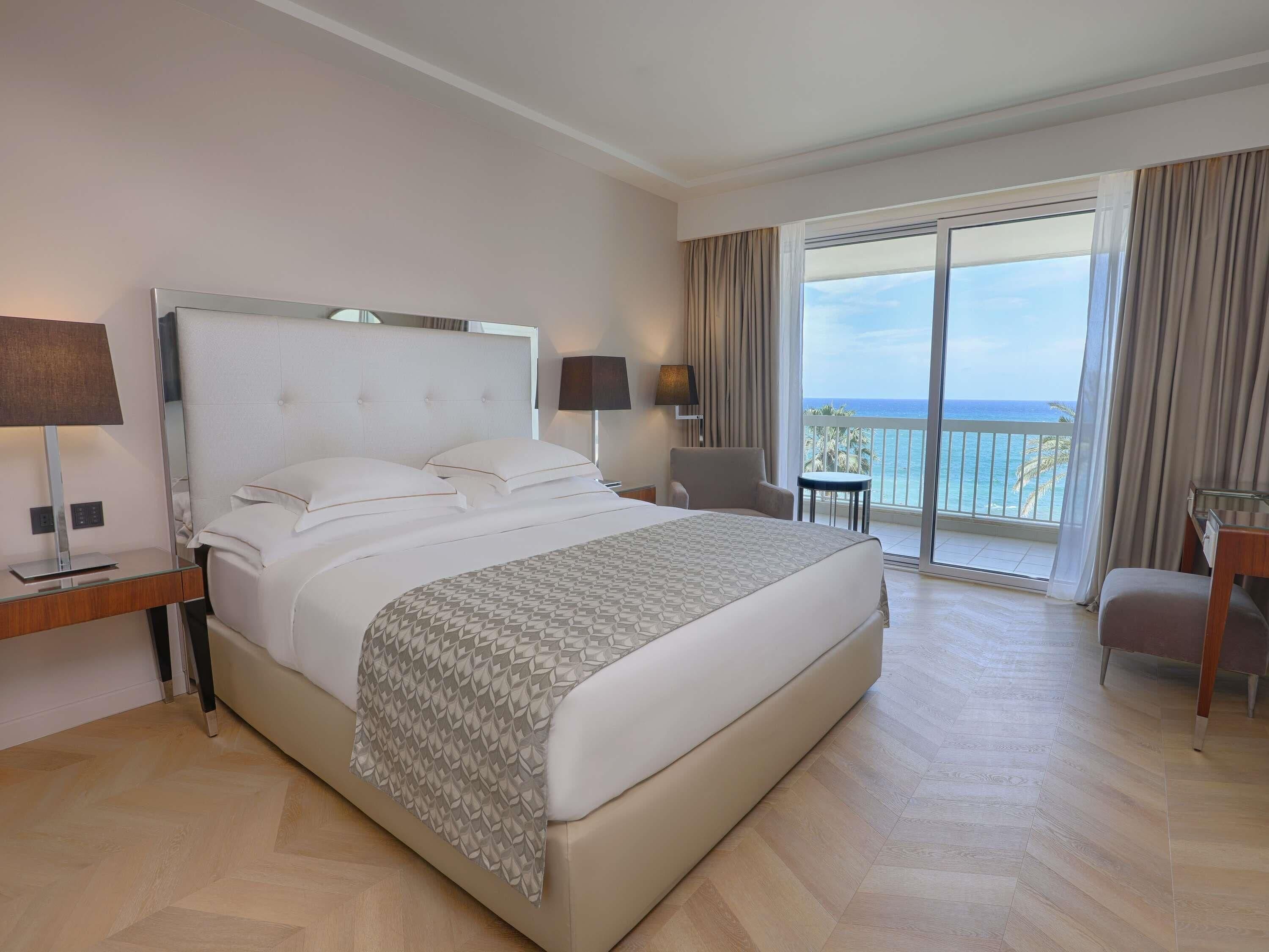 Habitación de hotel con una cama grande, un escritorio, una silla y un balcón con vista al océano.