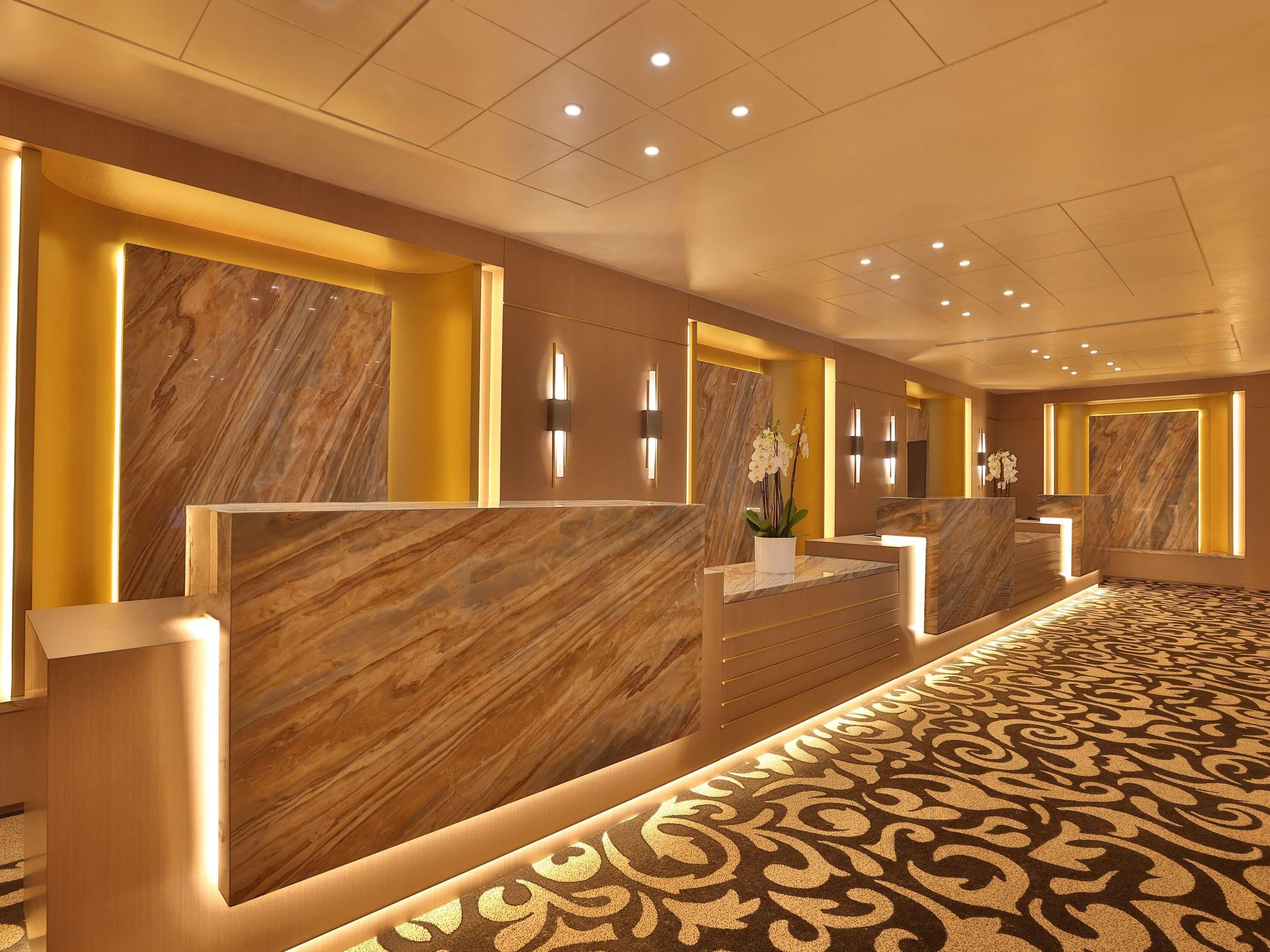 A hotel reception area with marble reception desks, a patterned carpet, and wall-mounted lighting.