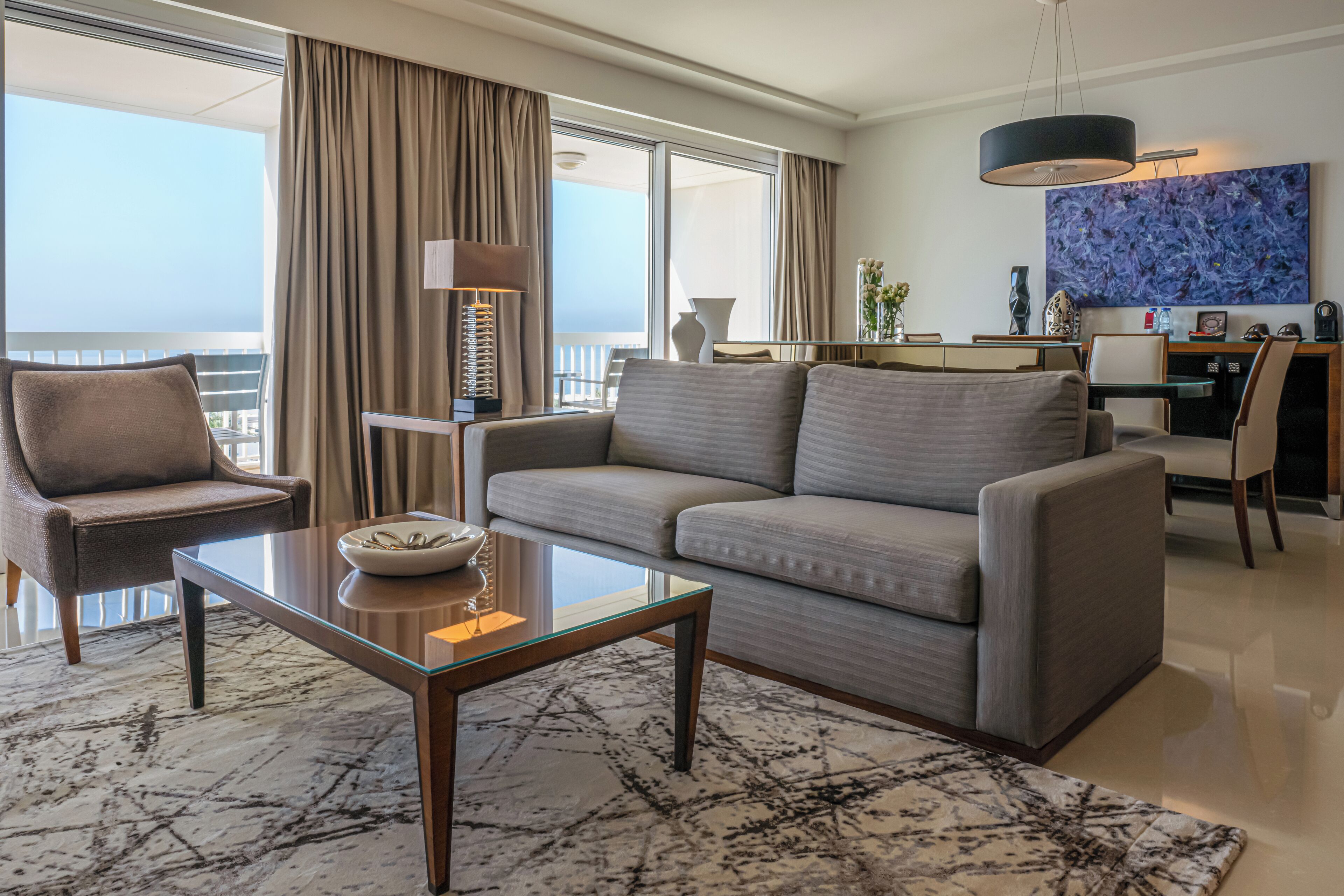 Ein modernes Hotelzimmer mit Balkon, einer Couch, einem Glastisch und einem Essbereich mit Aussicht.