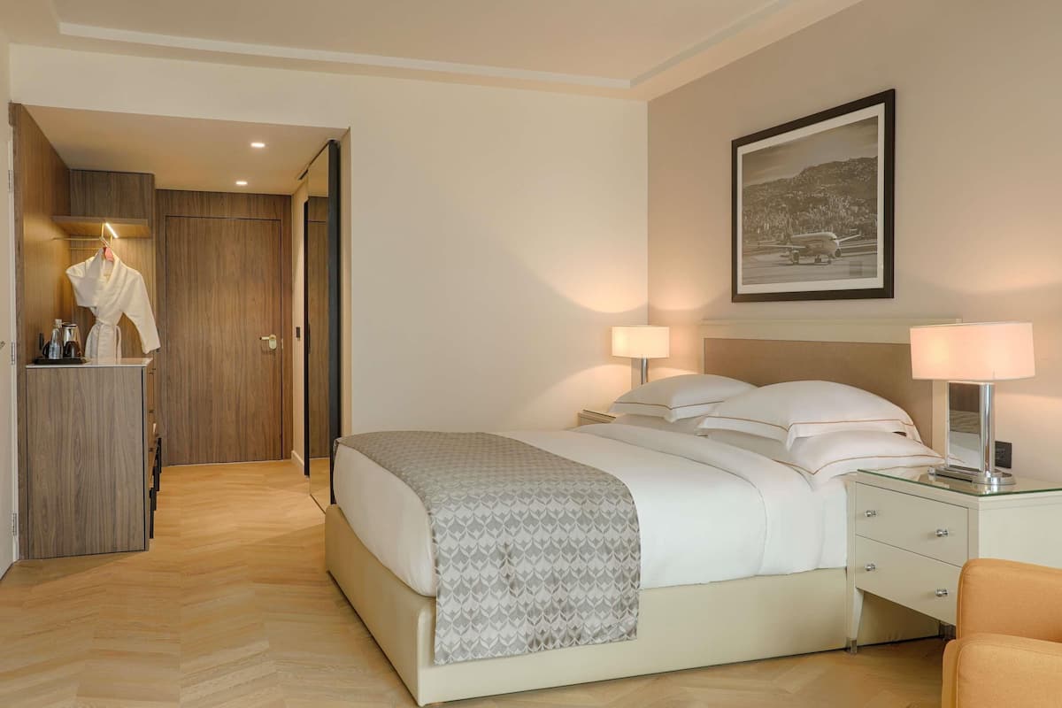 A hotel room with a bed, bedside lamps, a nightstand, a framed picture on the wall, and a wooden wardrobe.
