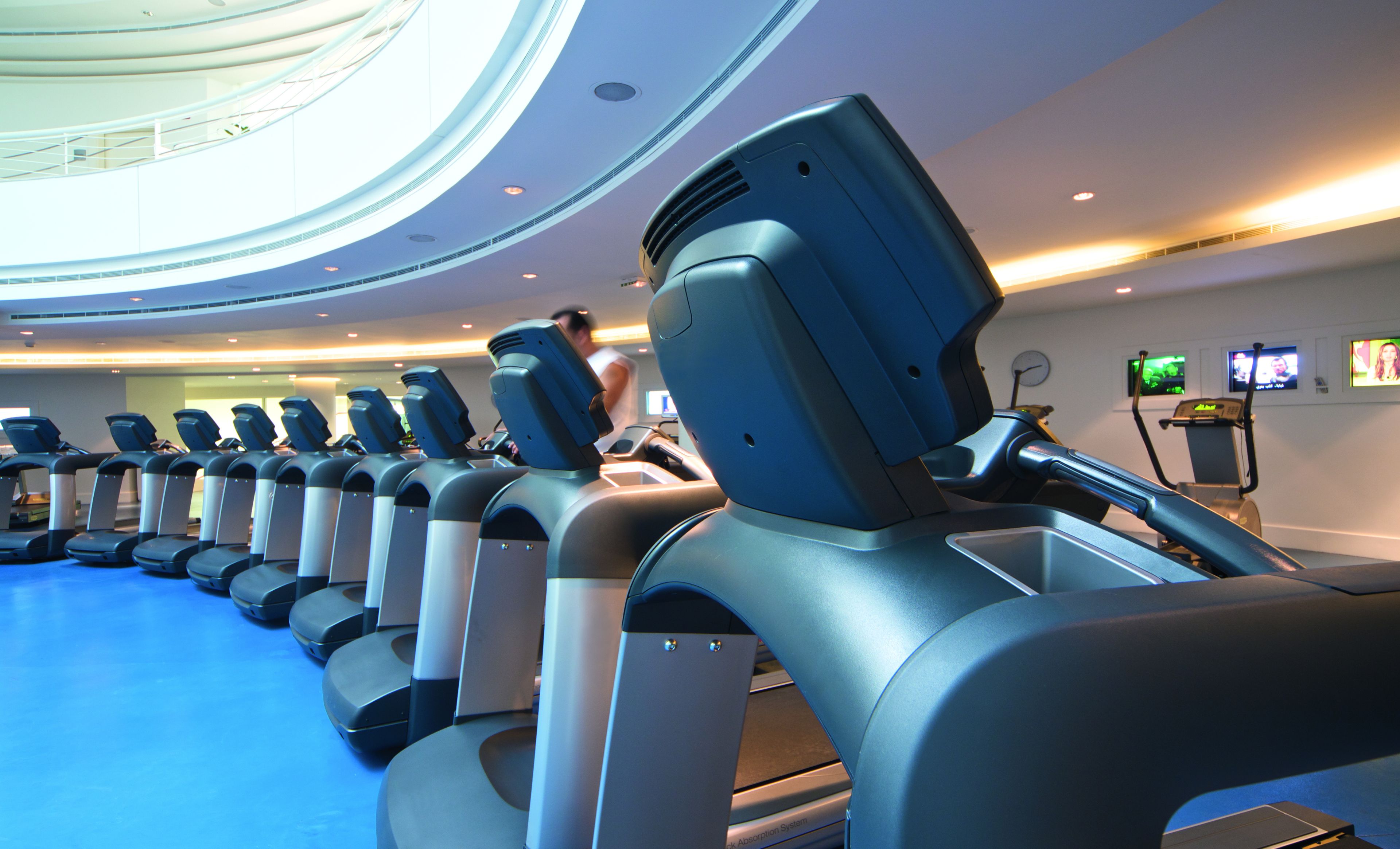 A row of stationary bikes in a gym with a high ceiling and a skylight.
