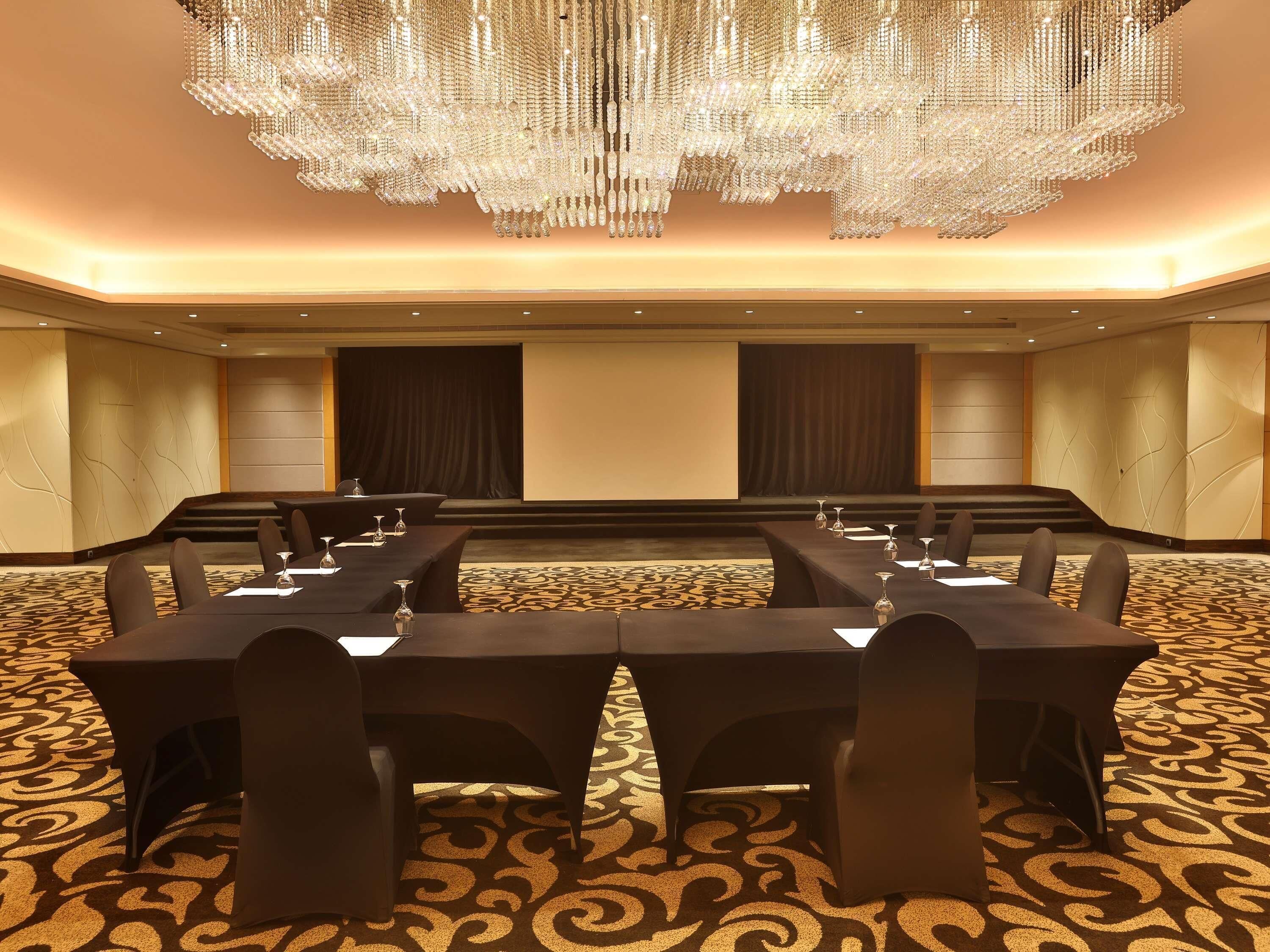 A conference room with a large chandelier, multiple tables with chairs, and a carpeted floor.