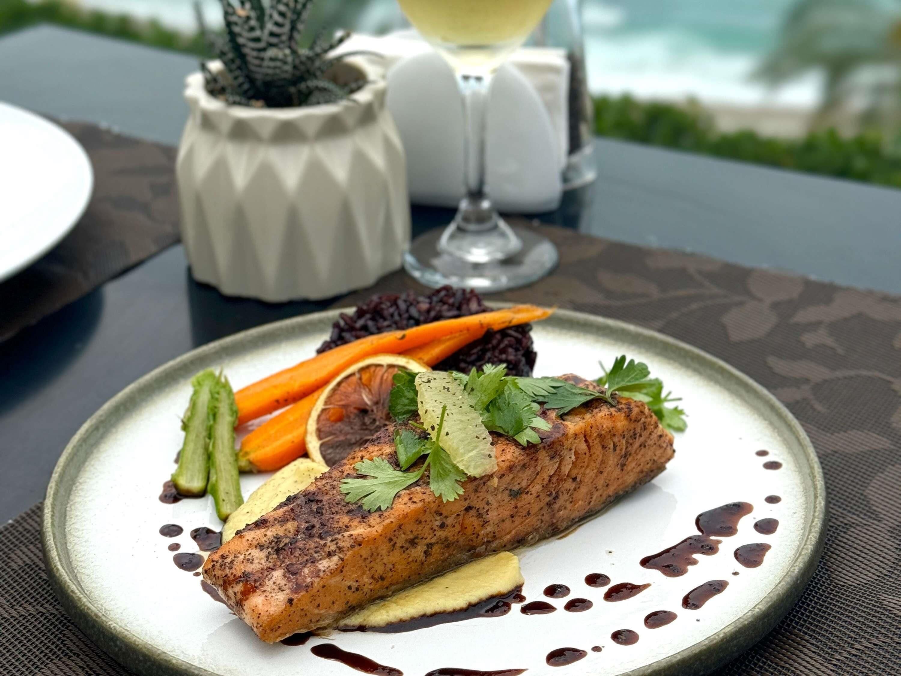 Un plato de comida con salmón, verduras y una copa de vino sobre una mesa.