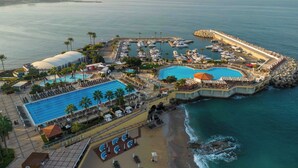 An aerial view of a coastal resort with multiple swimming pools, a beach area, and a marina. - Mövenpick Hotel Beirut (Beirut)