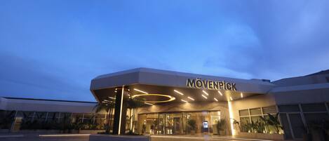 A modern hotel entrance with a large sign reading "MÖVENPICK" and a well-lit, paved driveway leading to the entrance.