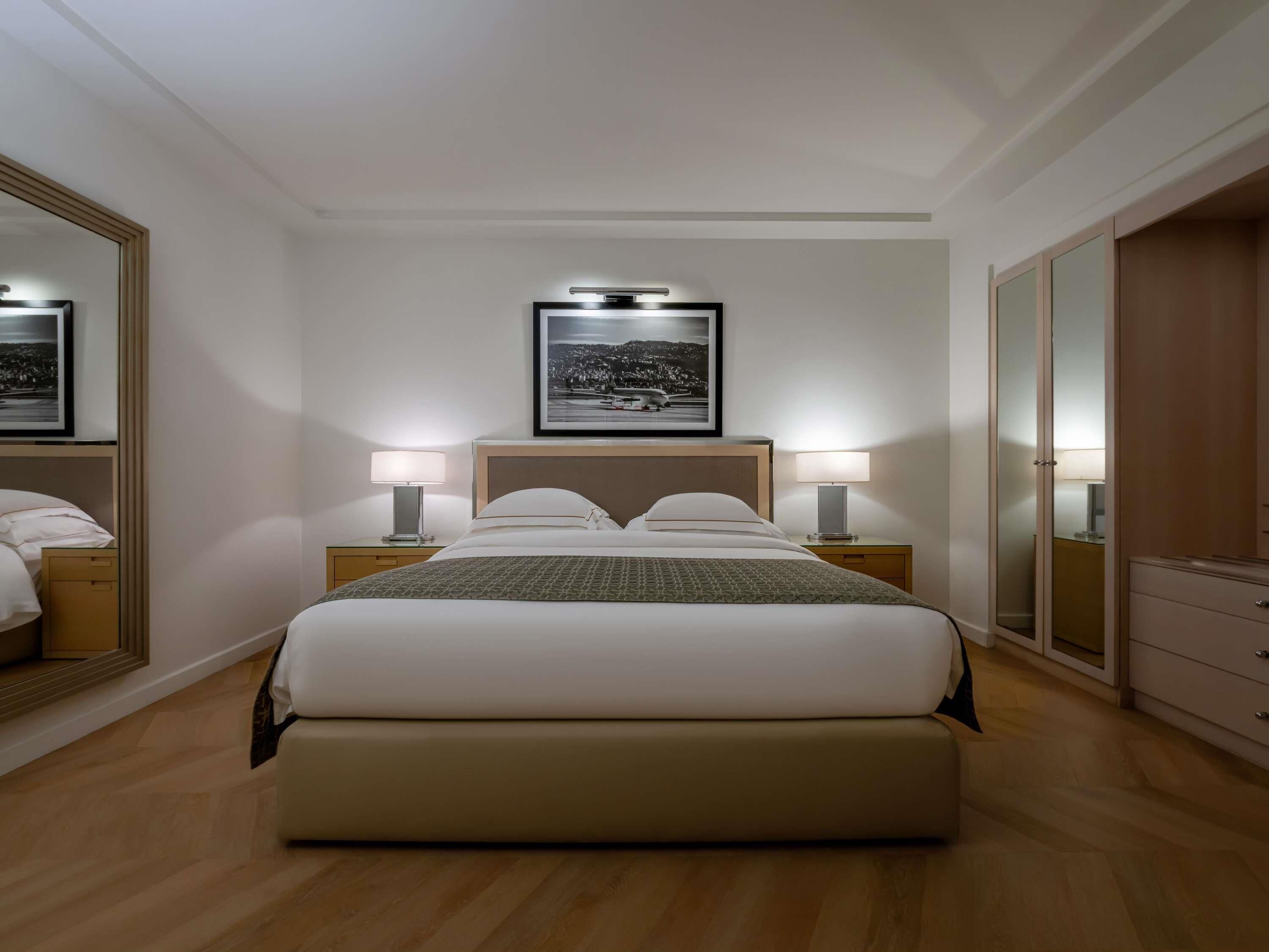 Una camera d'albergo con un letto grande, due comodini con lampade, un quadro incorniciato sopra il letto e un armadio.