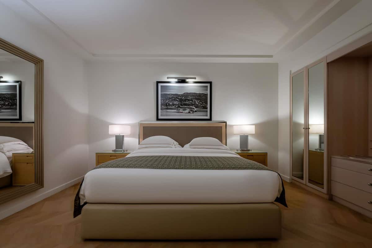 A hotel room with a large bed, two bedside tables with lamps, a framed picture above the bed, and a wardrobe.