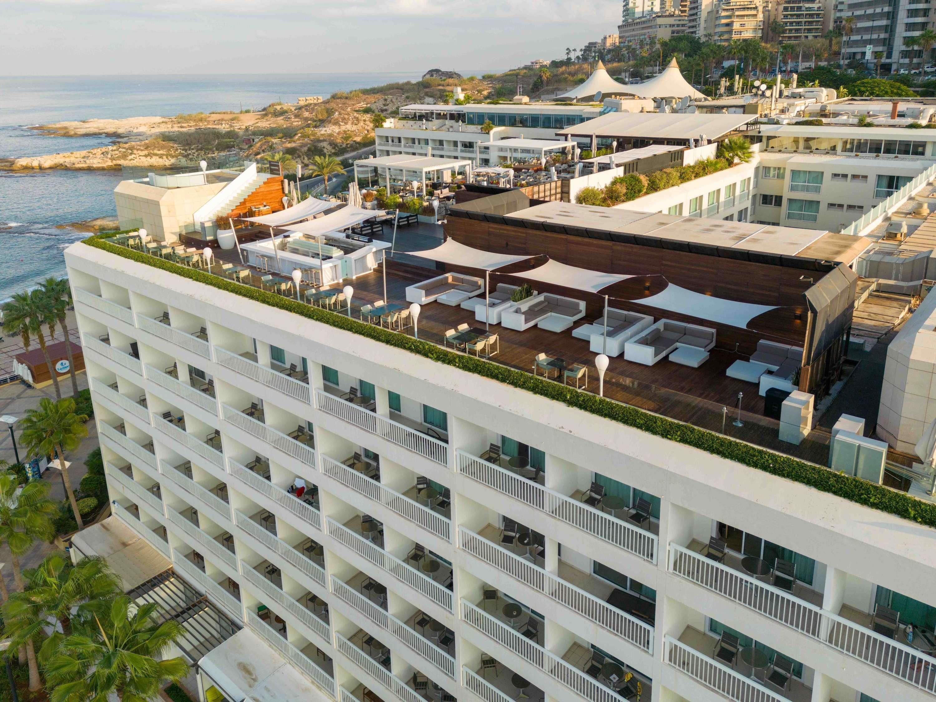 Un hotel moderno de gran altura con múltiples balcones, zonas de estar al aire libre y vistas a la costa.