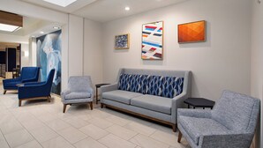 Un vestíbulo moderno con un sofá gris, sillones azules y un sillón estampado.