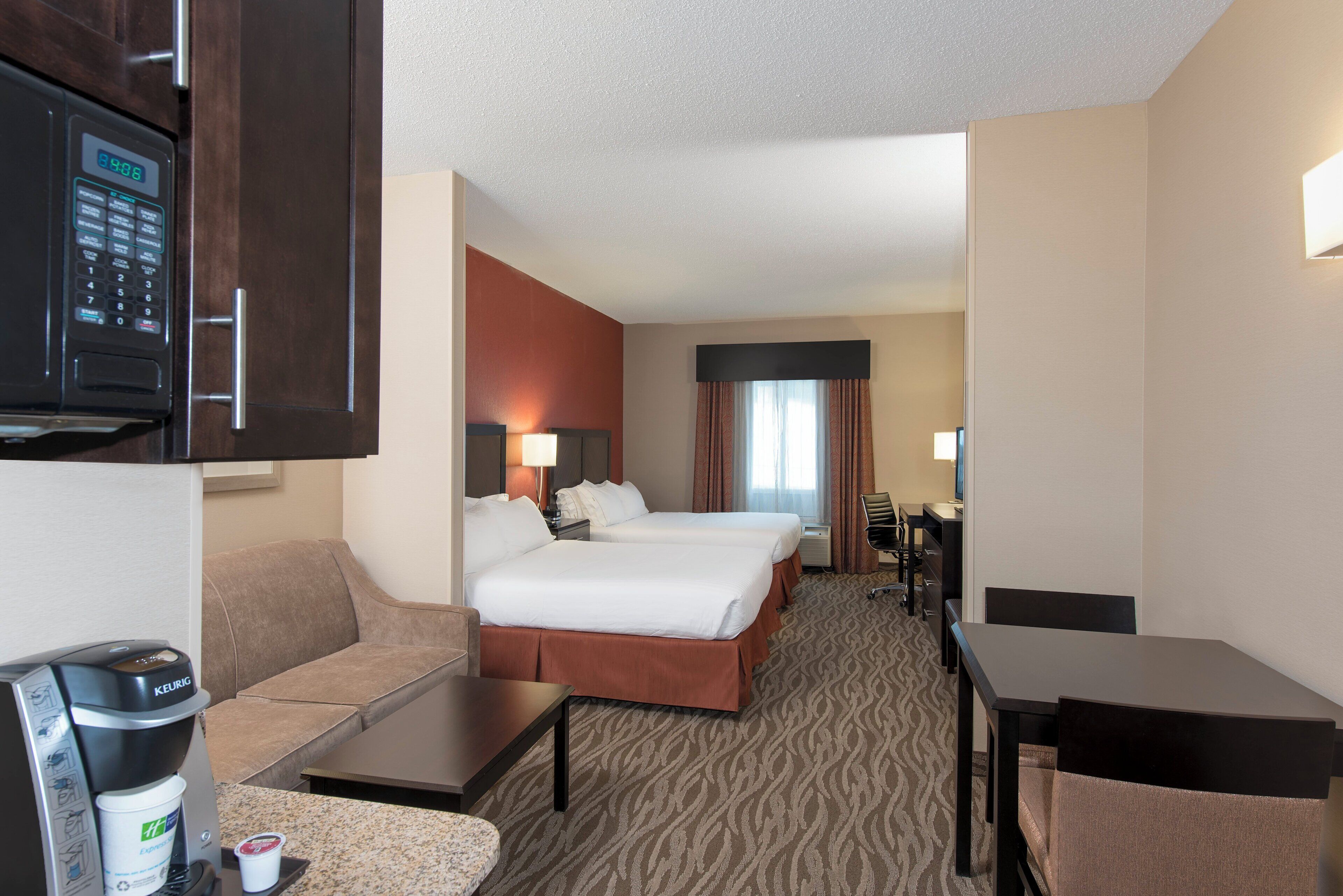 A hotel room with two beds, a kitchenette, a seating area, and a television.