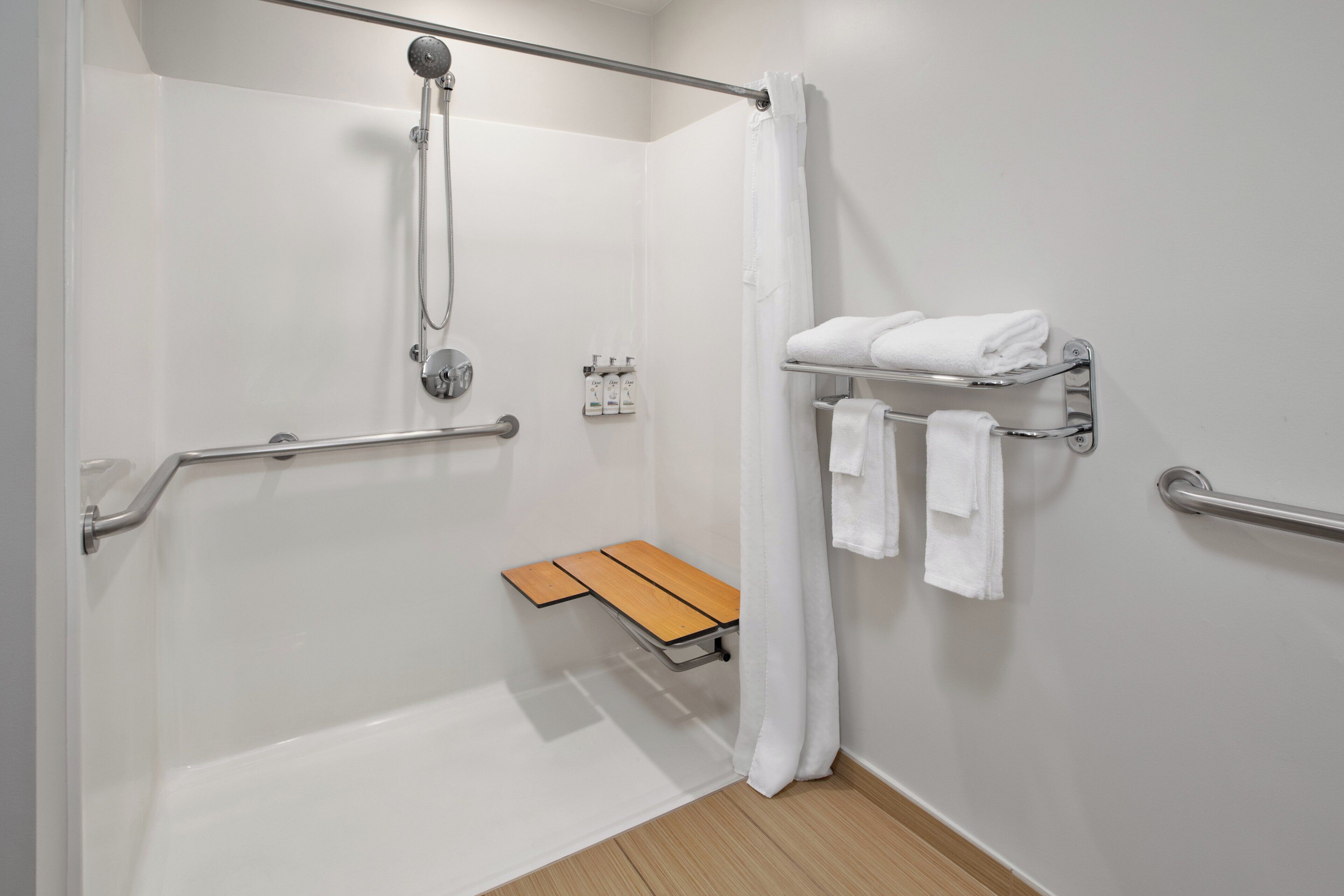 Un baño moderno con ducha, barras de apoyo, un banco y un perchero para toallas.