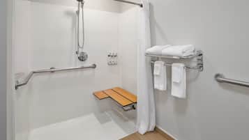 Un baño moderno con ducha, barras de apoyo, un banco y un perchero para toallas.