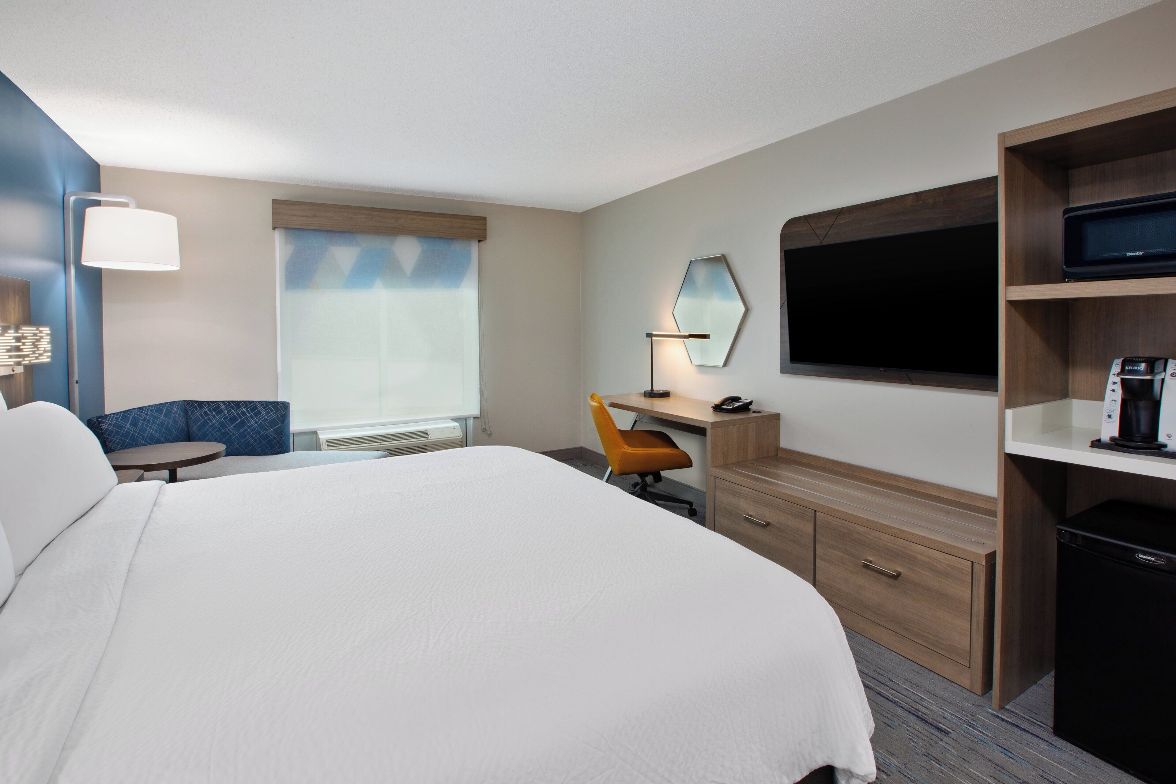 A hotel room with a large bed, a desk with a chair, a TV, and a minibar.