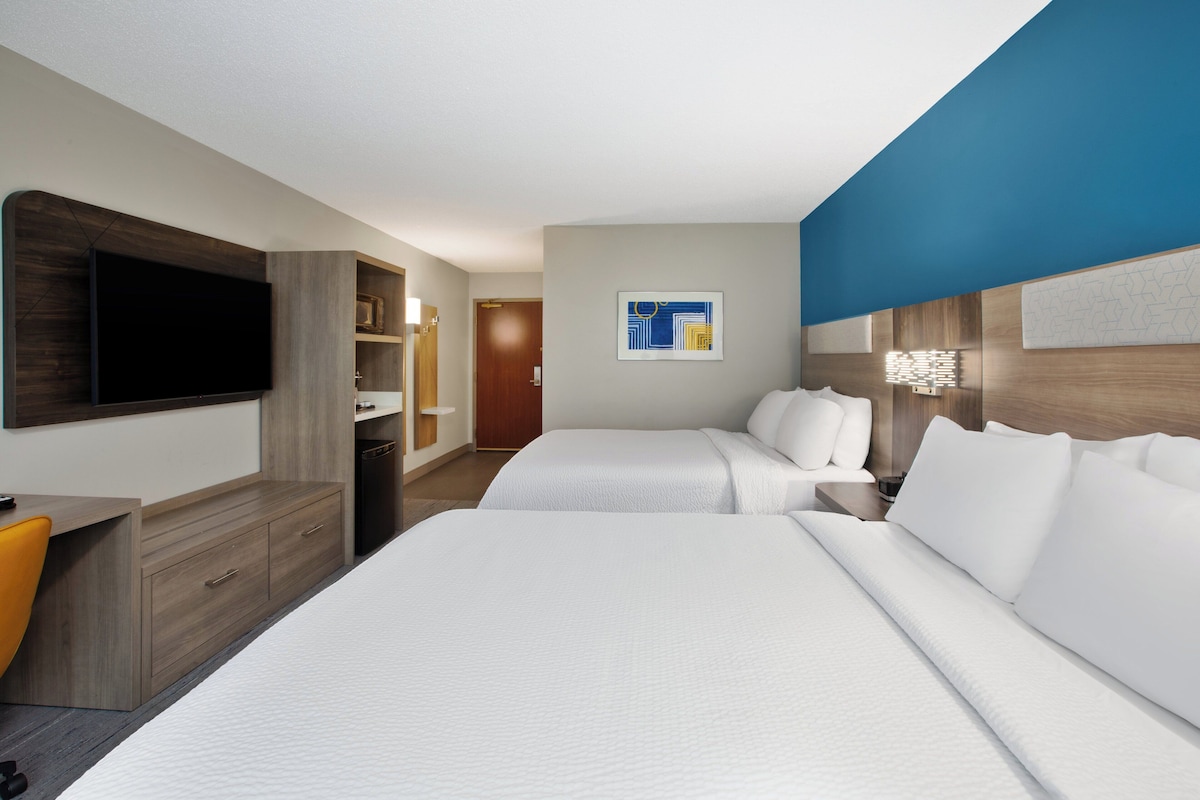 A hotel room with two beds, a TV, a desk, and a bathroom.