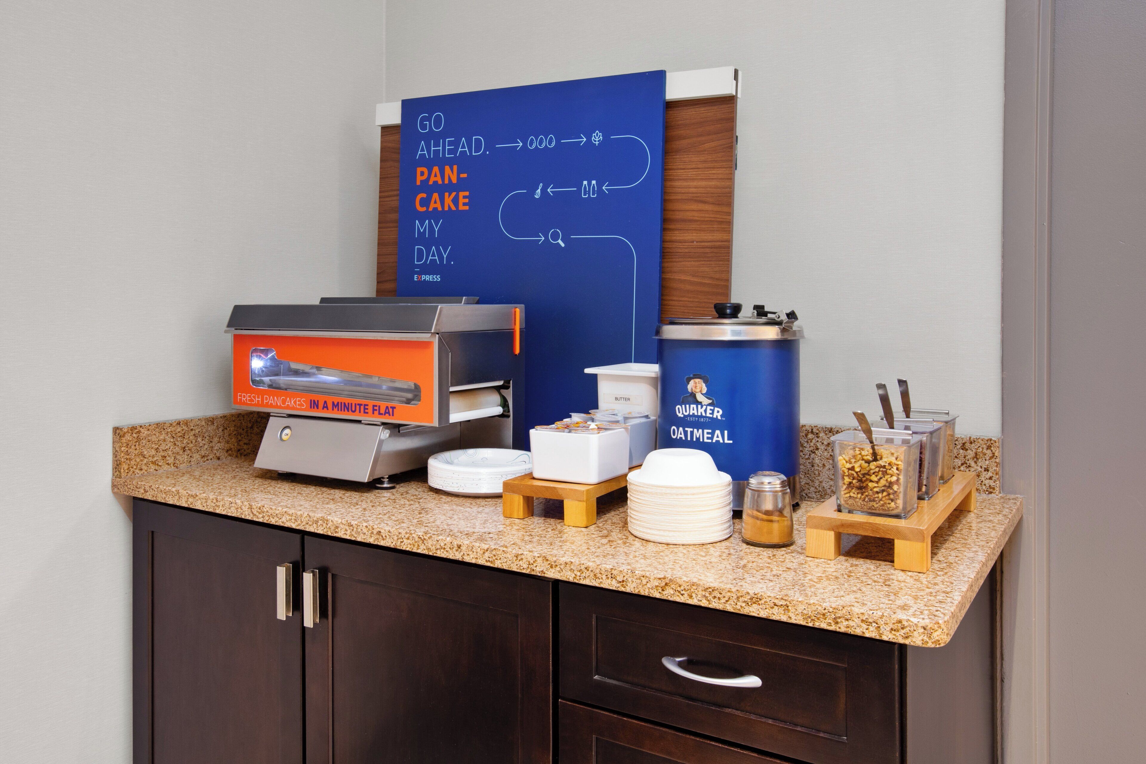A breakfast bar with a coffee machine, a waffle maker, a container of oatmeal, and a jar of honey.