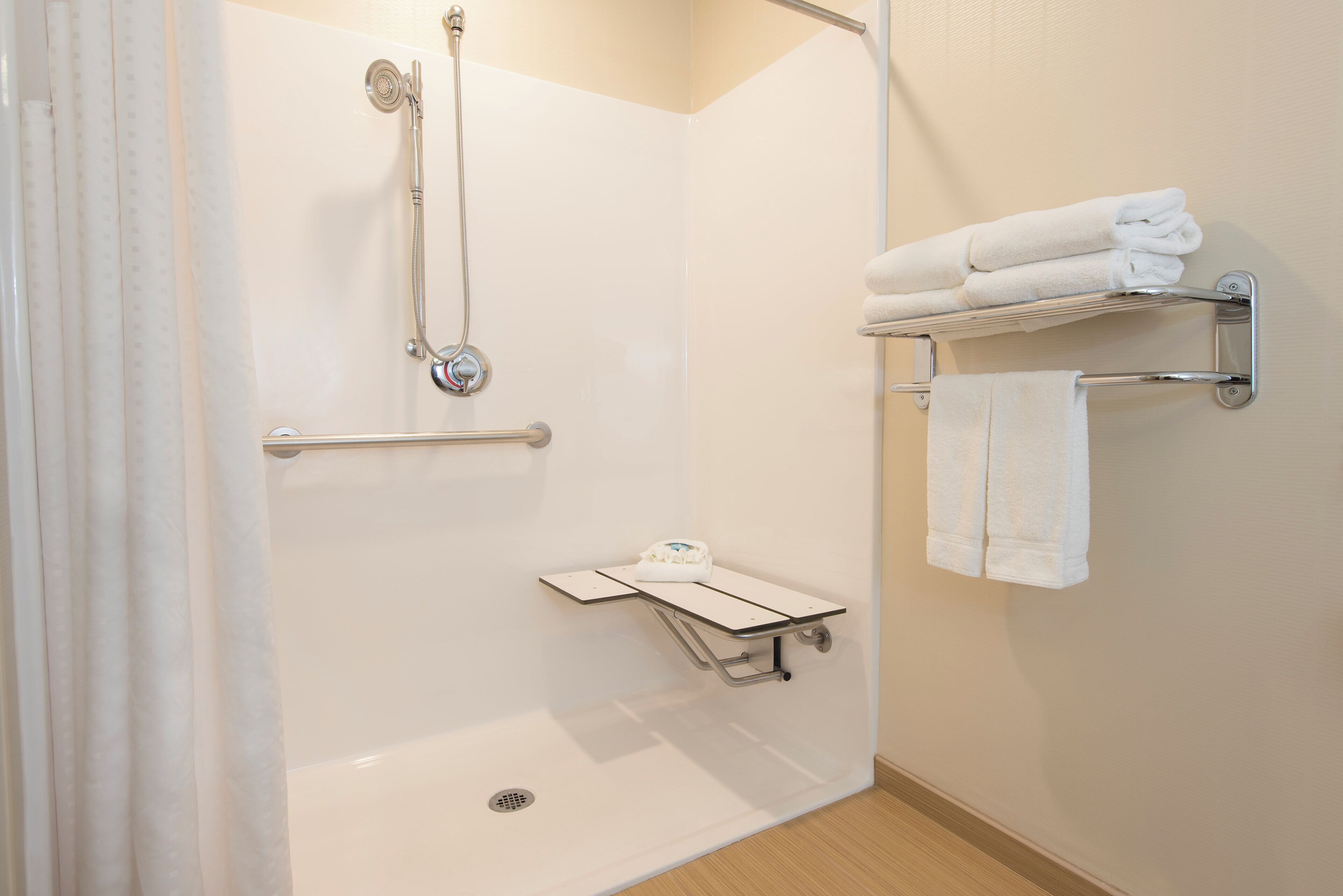A modern bathroom with a walk-in shower, grab bars, a towel rack, and a small shelf.