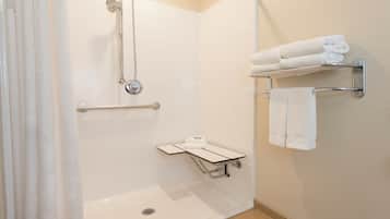 A modern bathroom with a walk-in shower, grab bars, a towel rack, and a small shelf.