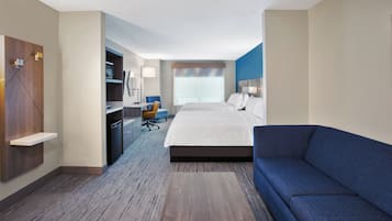 Una habitación de hotel con una cama grande, un sofá azul, un escritorio con una silla, un armario y una ventana con persianas.