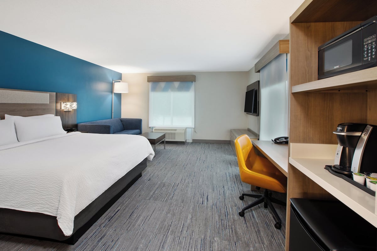 Habitación de hotel con cama, escritorio, silla, microondas, cafetera y televisor.