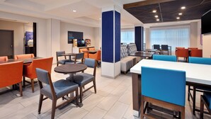 Un moderno vestíbulo de hotel con varias zonas de estar, incluidas mesas y sillas, y una estación de café.