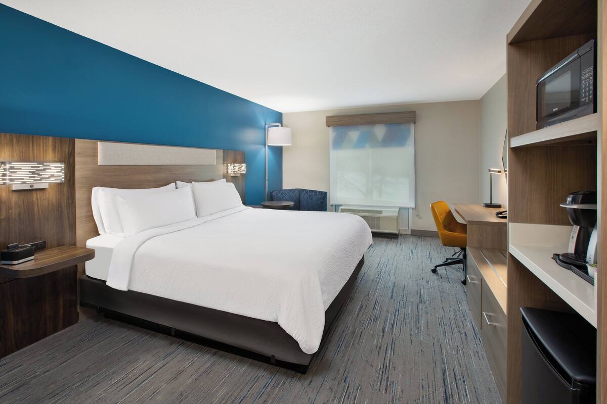 Una habitación de hotel con una cama grande, un escritorio, una silla, un microondas y una cafetera.