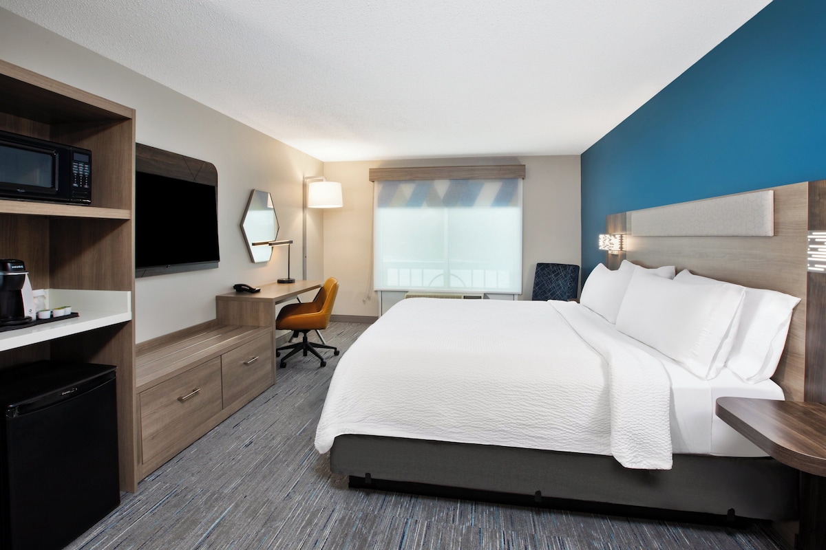A hotel room with a bed, a desk, a chair, a TV, and a minibar.