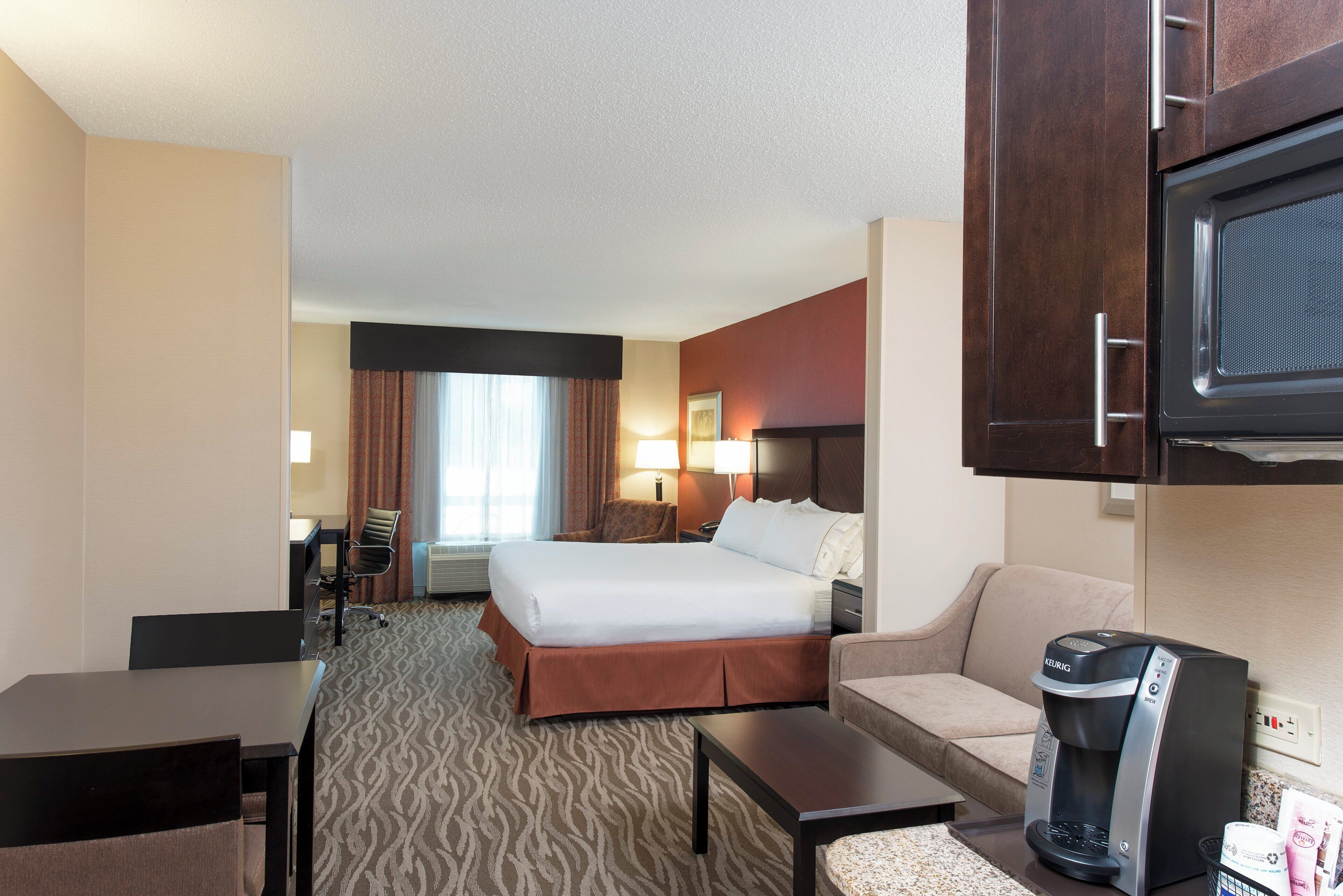 A hotel room with a bed, a desk, a chair, a sofa, a coffee maker, and a television.