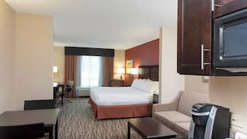 A hotel room with a bed, a desk, a chair, a sofa, a coffee maker, and a television.