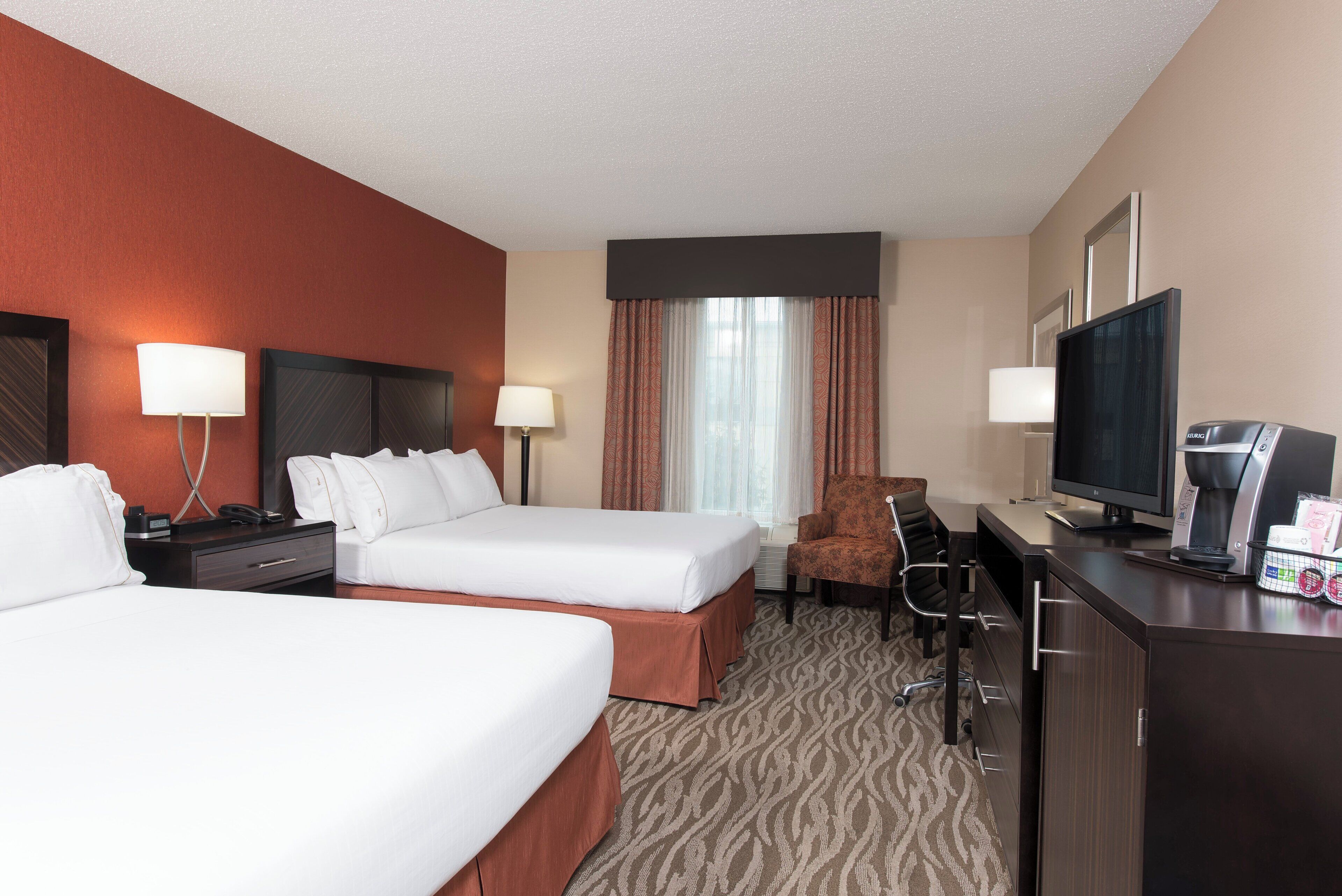 A hotel room with two beds, a desk with a television, a coffee maker, and a chair.