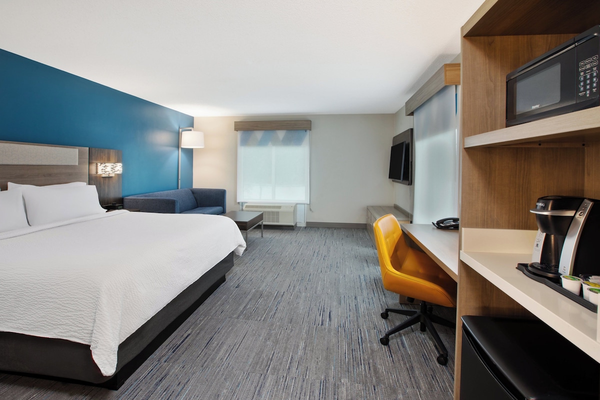 A hotel room with a bed, a desk, a chair, a microwave, a coffee maker, and a TV.