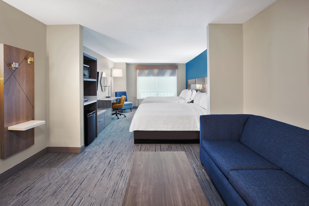 Una habitación de hotel con una cama grande, un sofá azul, un escritorio con una silla, un armario y una ventana con persianas.