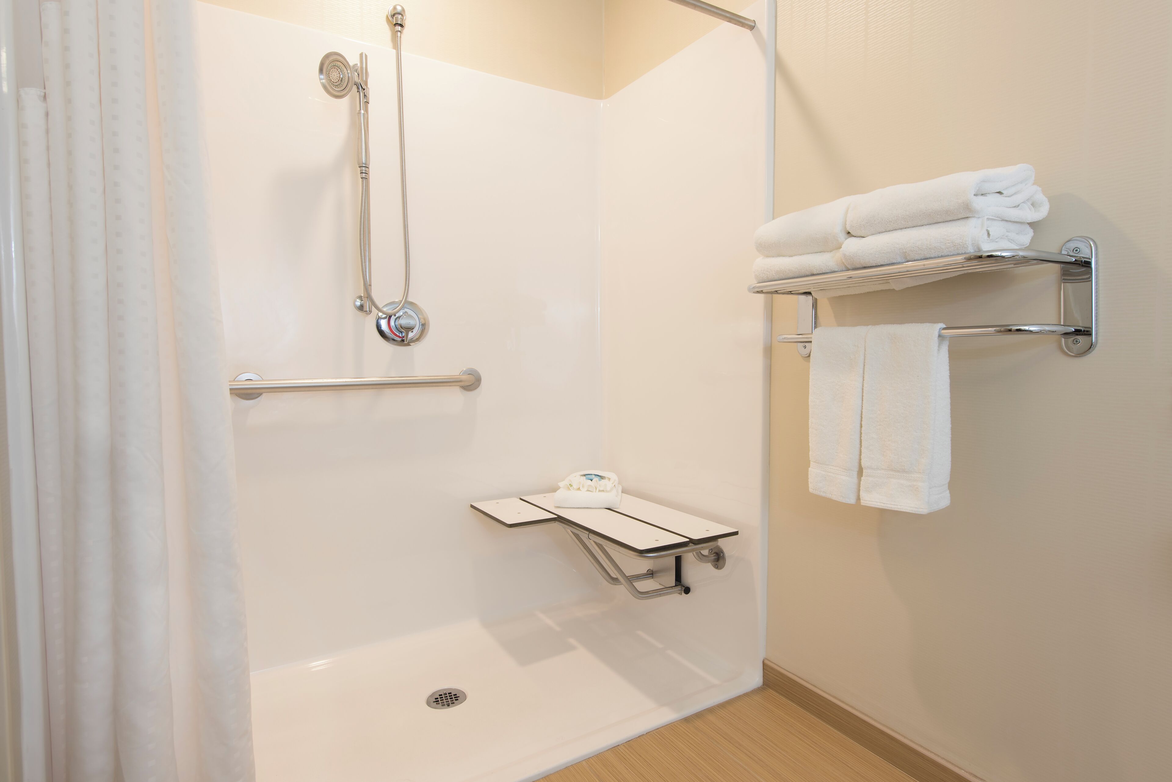 A modern bathroom with a walk-in shower, grab bars, a towel rack, and a small shelf.