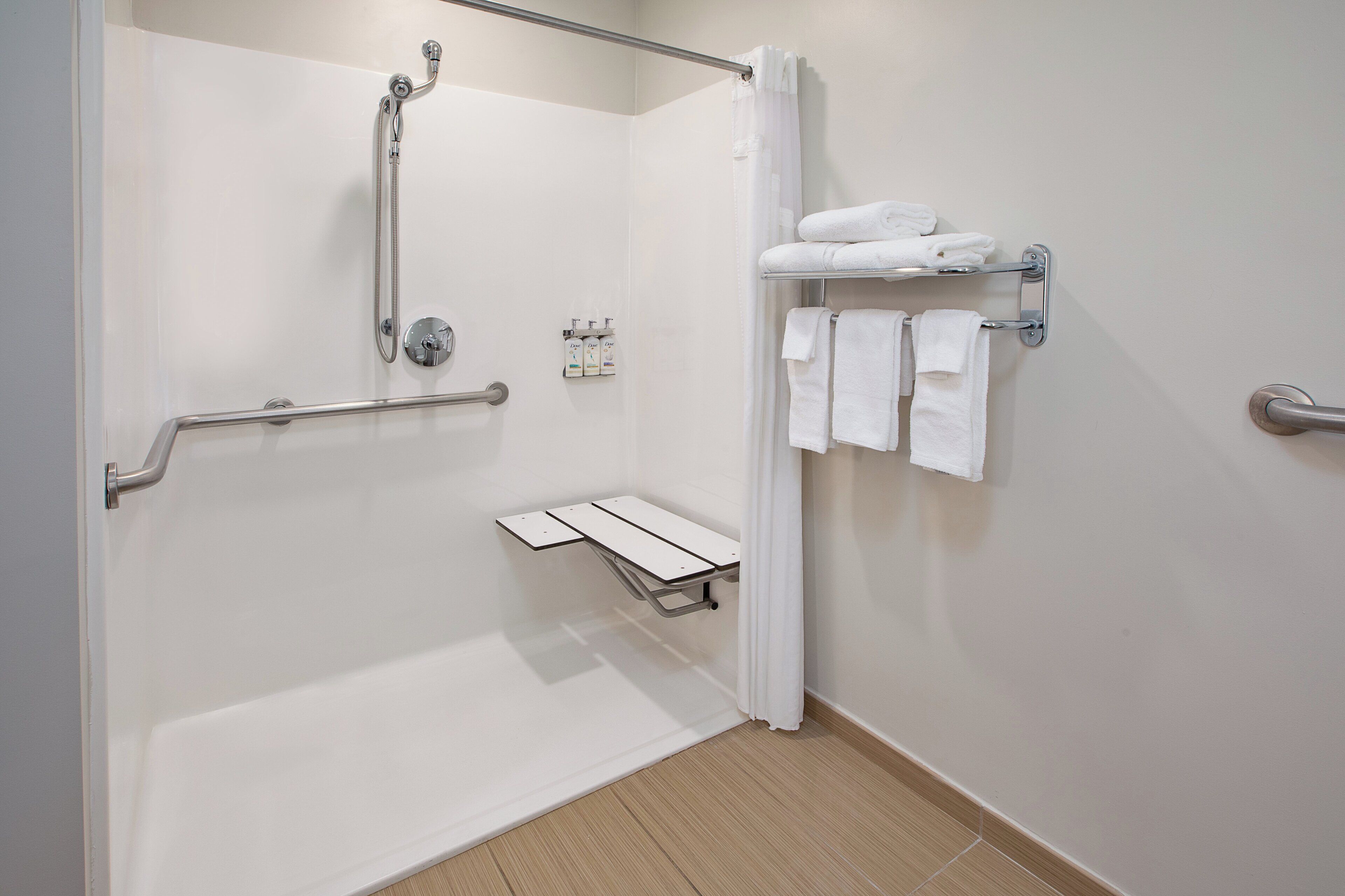 A modern bathroom with a walk-in shower, grab bars, a towel rack, and a small shelf.