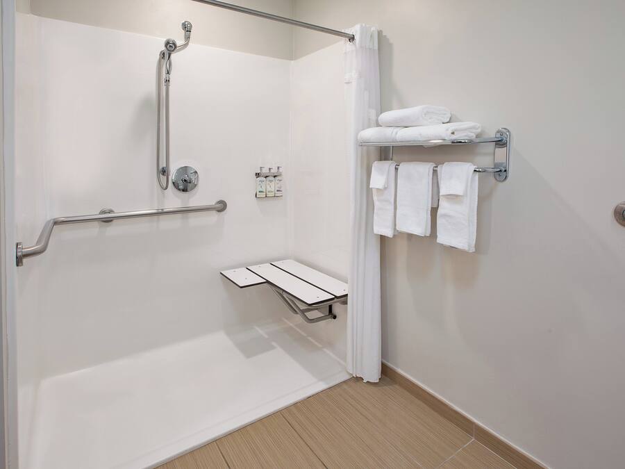 A modern bathroom with a walk-in shower, grab bars, a towel rack, and a small shelf.