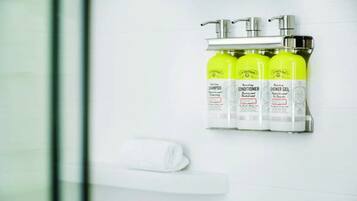 A bathroom with a white towel on a rack, three bottles of shower gel, and a faucet.
