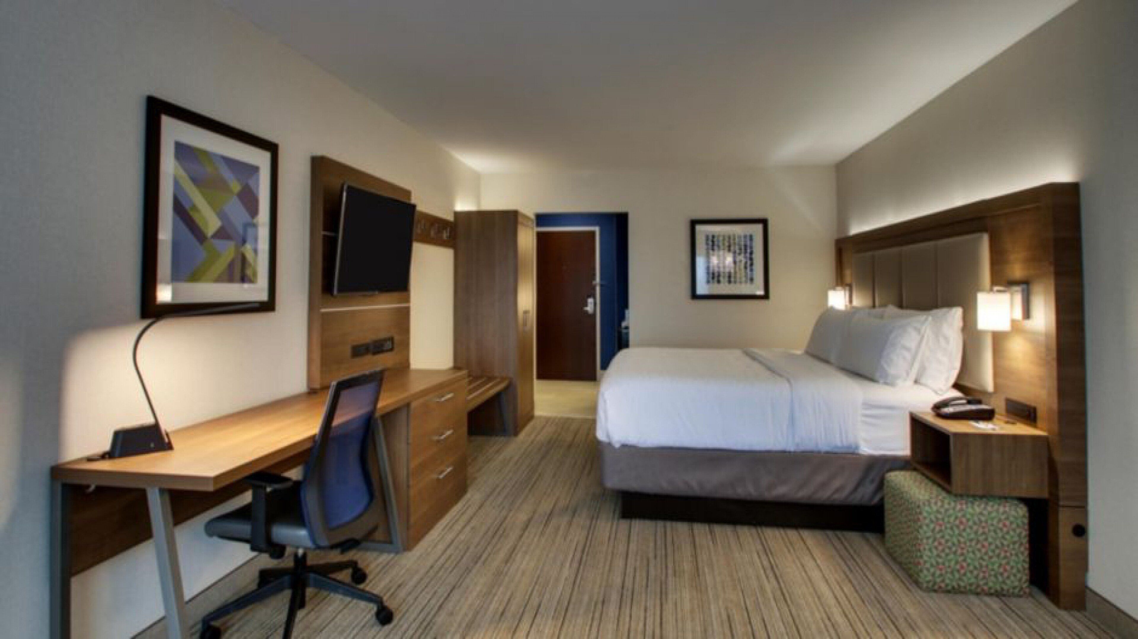 Een hotelkamer met een bed, bureau, stoel, televisie en kunstwerk.