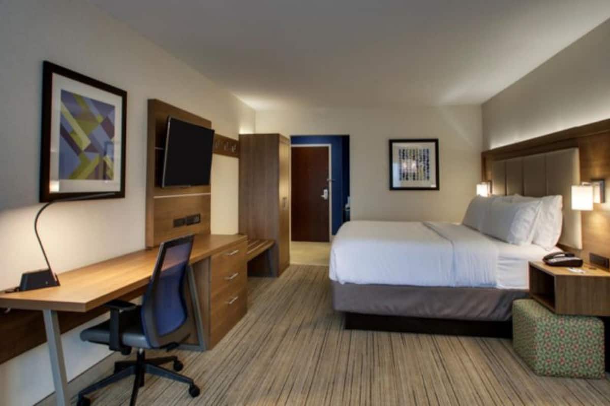 Une chambre d’hôtel équipée d’un lit, d’un bureau, d’une chaise, d’une télévision et décorée avec des œuvres d’art aux murs.
