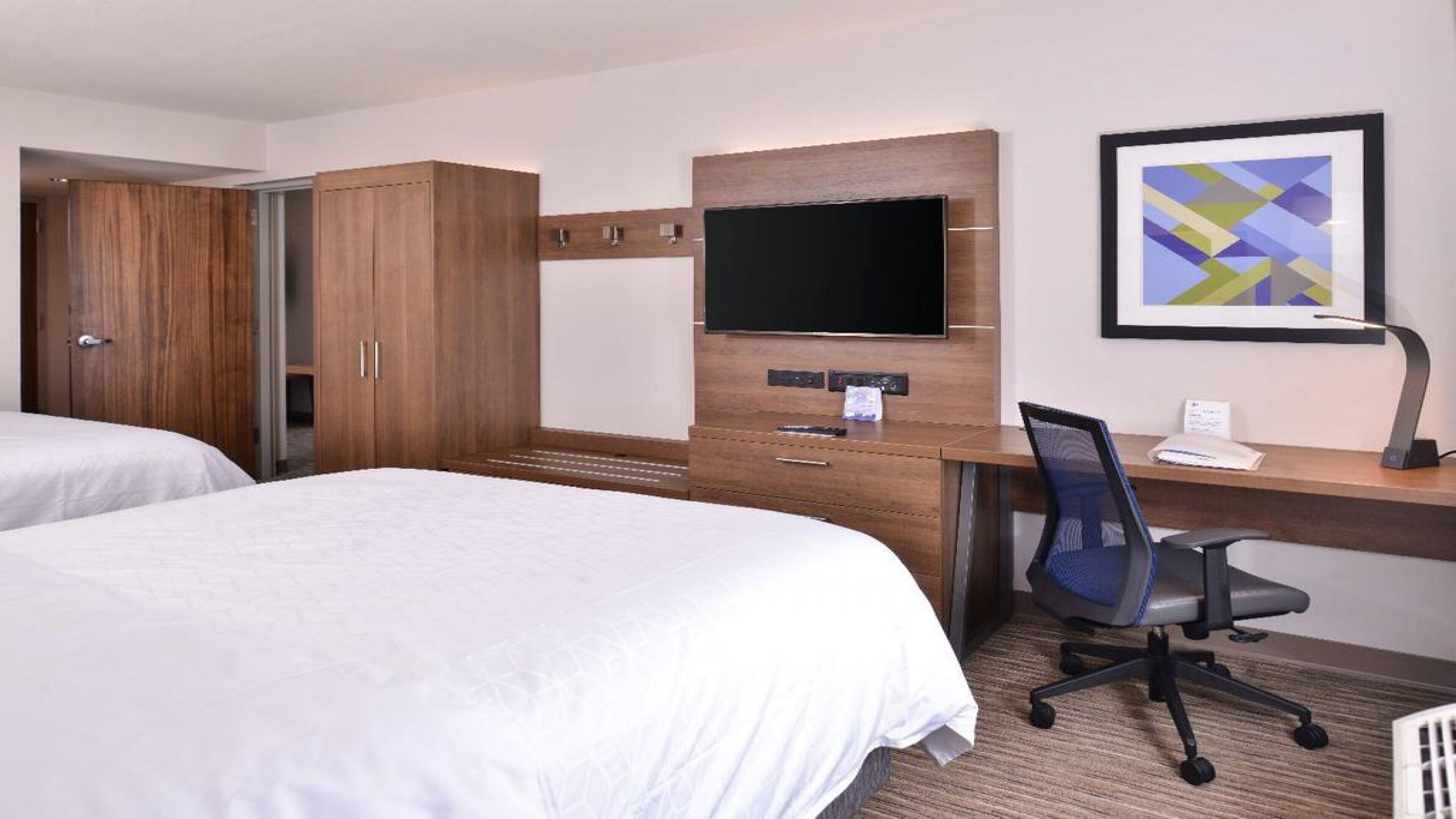 A hotel room with two beds, a desk with a computer, a TV, and a framed picture on the wall.