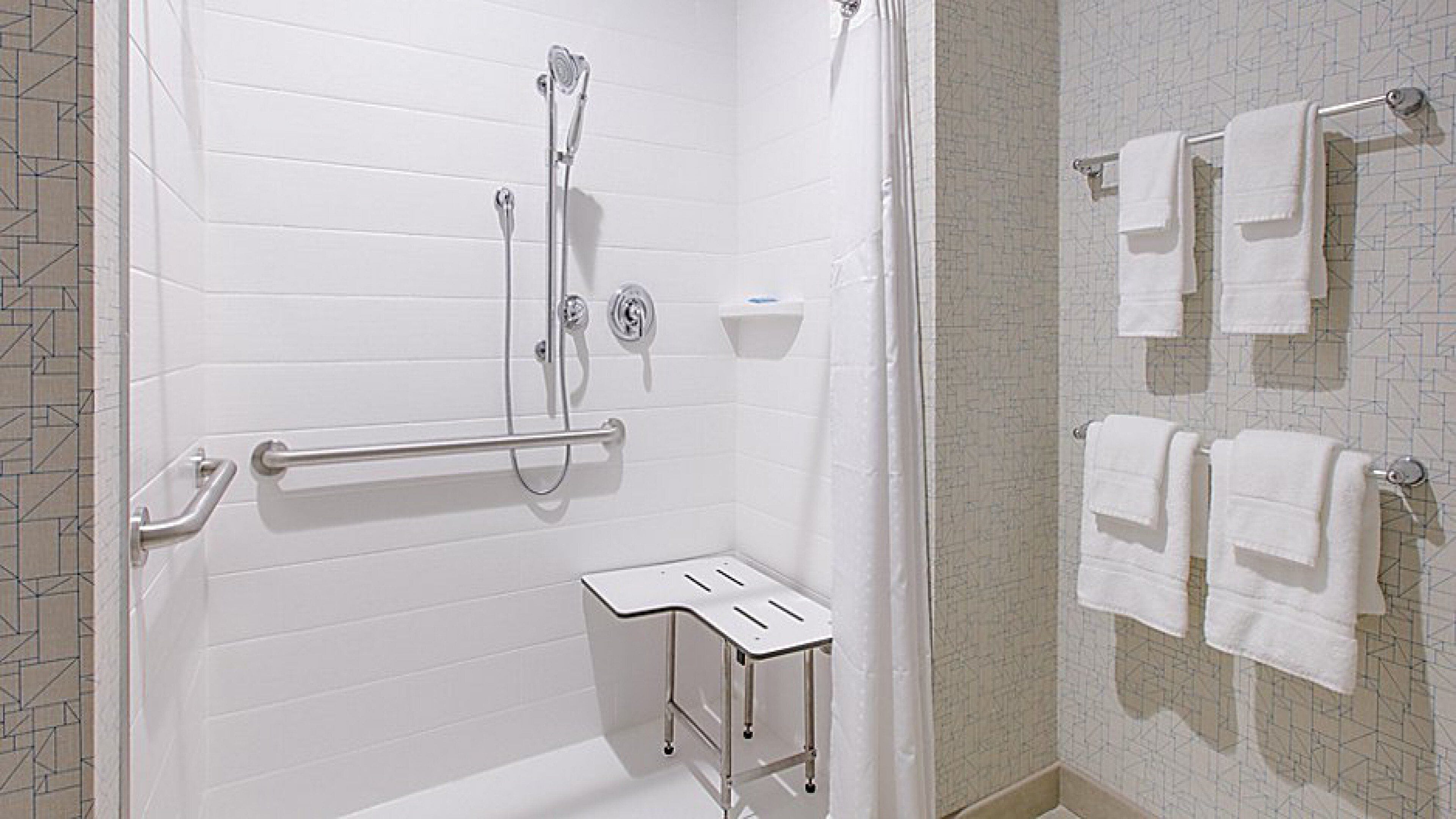 A bathroom with a shower, grab bars, a towel rack, and a small step stool.