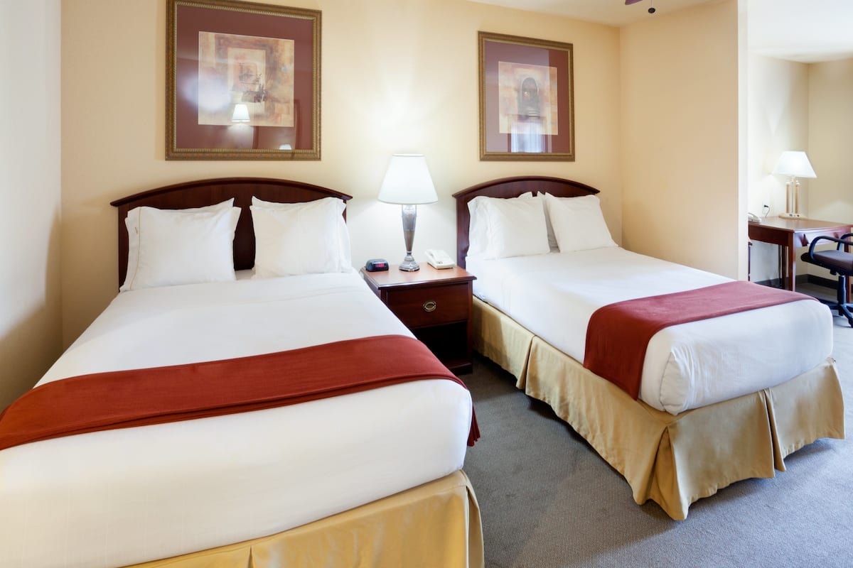A hotel room with two beds, each with white linens and red accents, a bedside table with a lamp, and framed artwork on the walls.