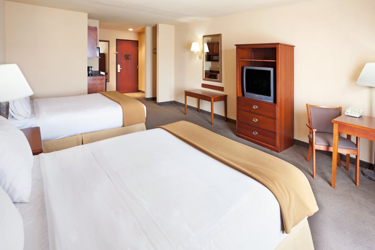 A hotel room with two beds, a desk, a television, and a chair.