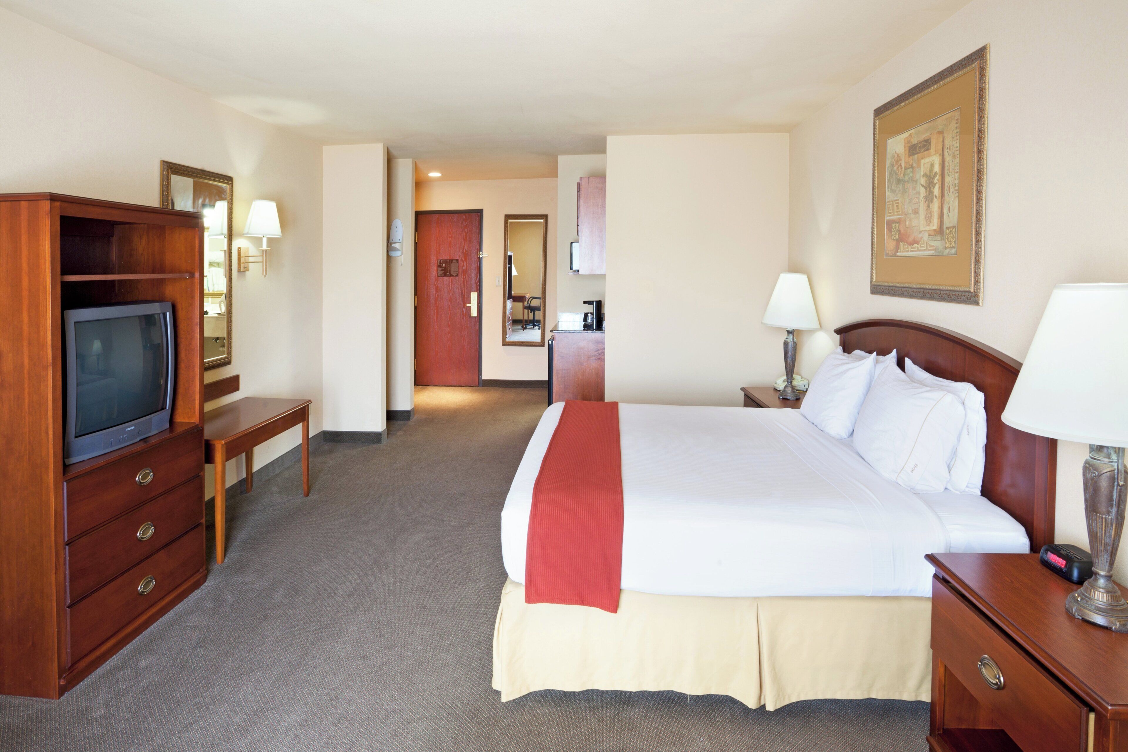 A hotel room with a bed, a TV, a desk, and a mirror.