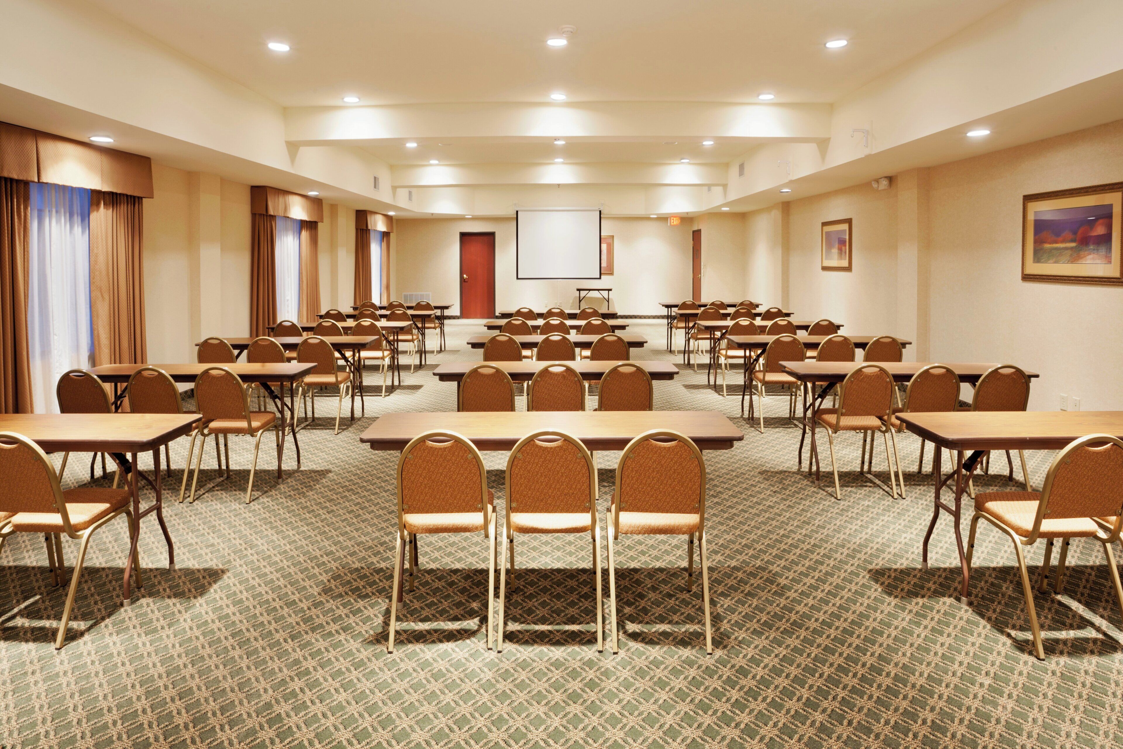 A conference room with multiple tables and chairs, a projector screen, and a door.