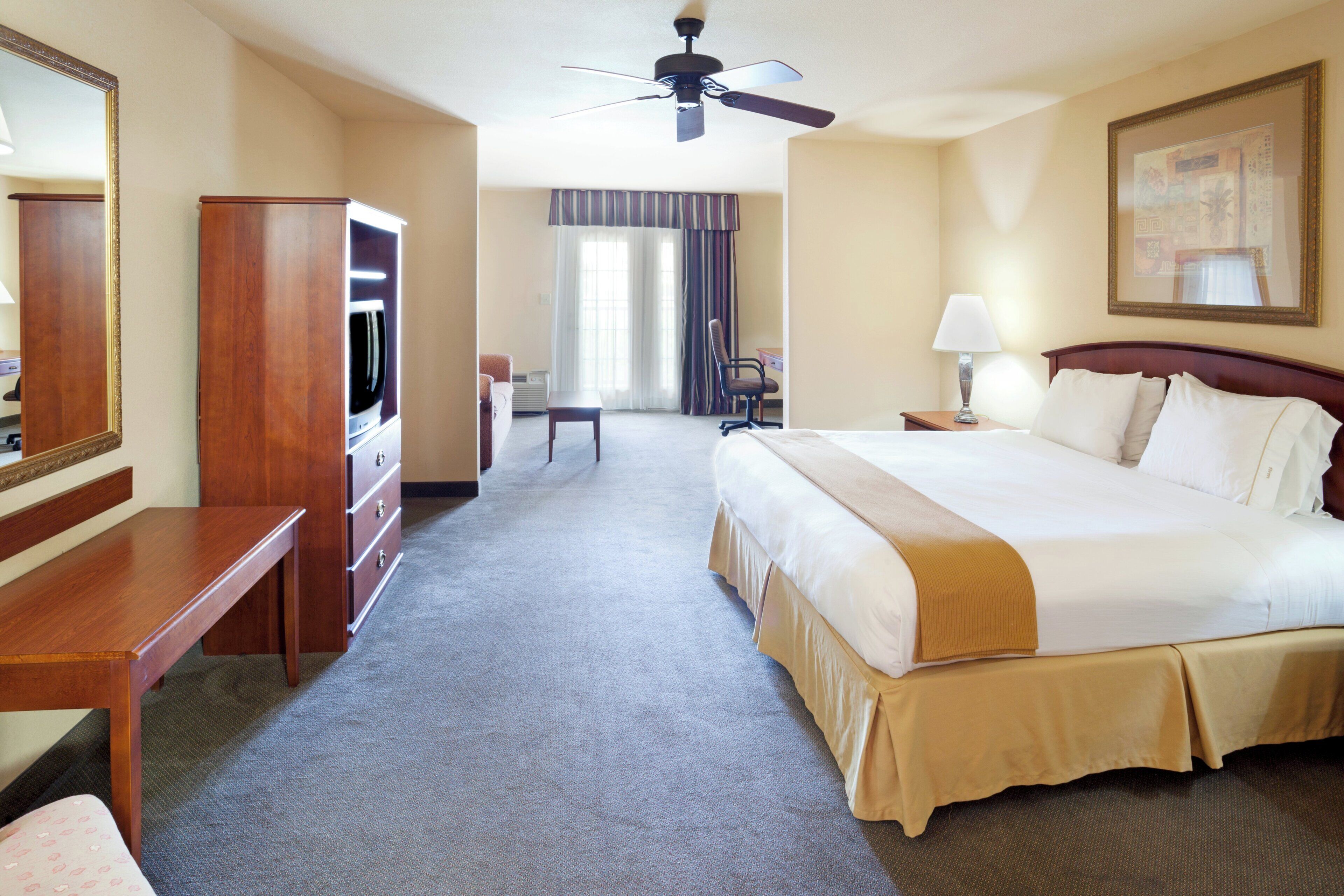 Ein Hotelzimmer mit Bett, Schreibtisch, Stuhl, Fernseher und Deckenventilator.