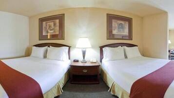 A hotel room with two beds, a nightstand with a lamp, and two framed pictures on the walls.