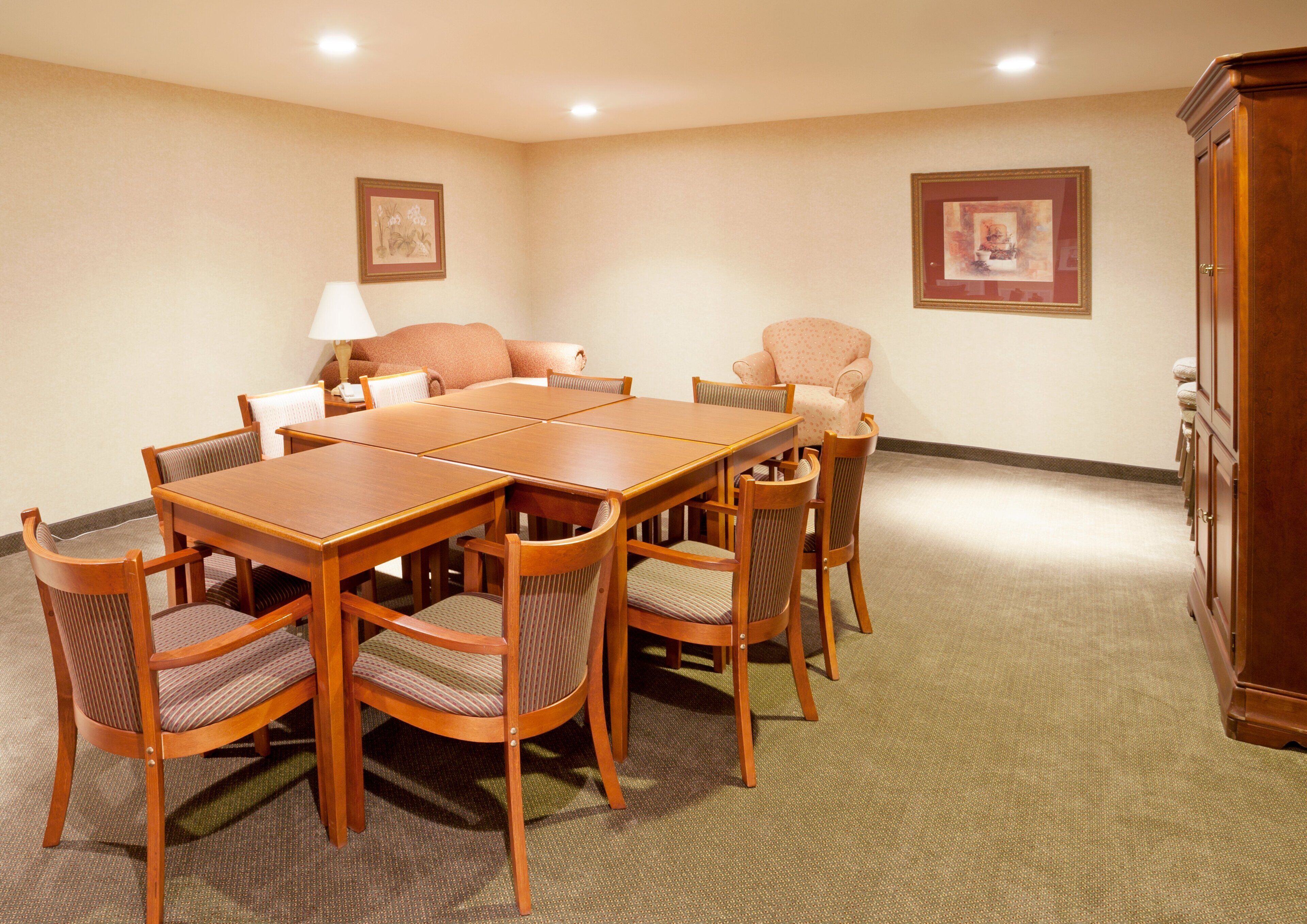 A conference room with a wooden table and chairs, a lamp, and two framed pictures on the walls.
