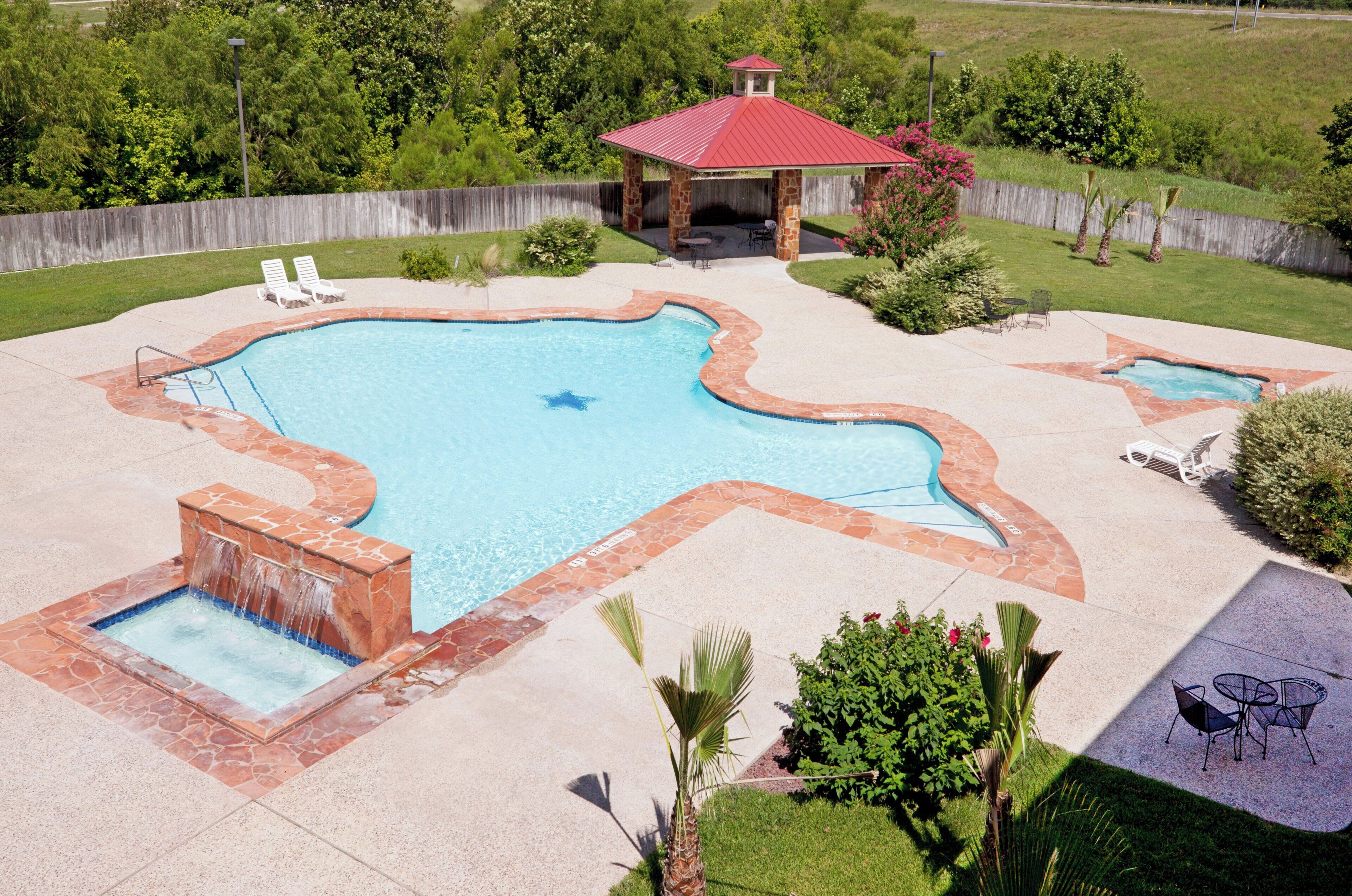 A backyard with a swimming pool, a hot tub, and a gazebo.