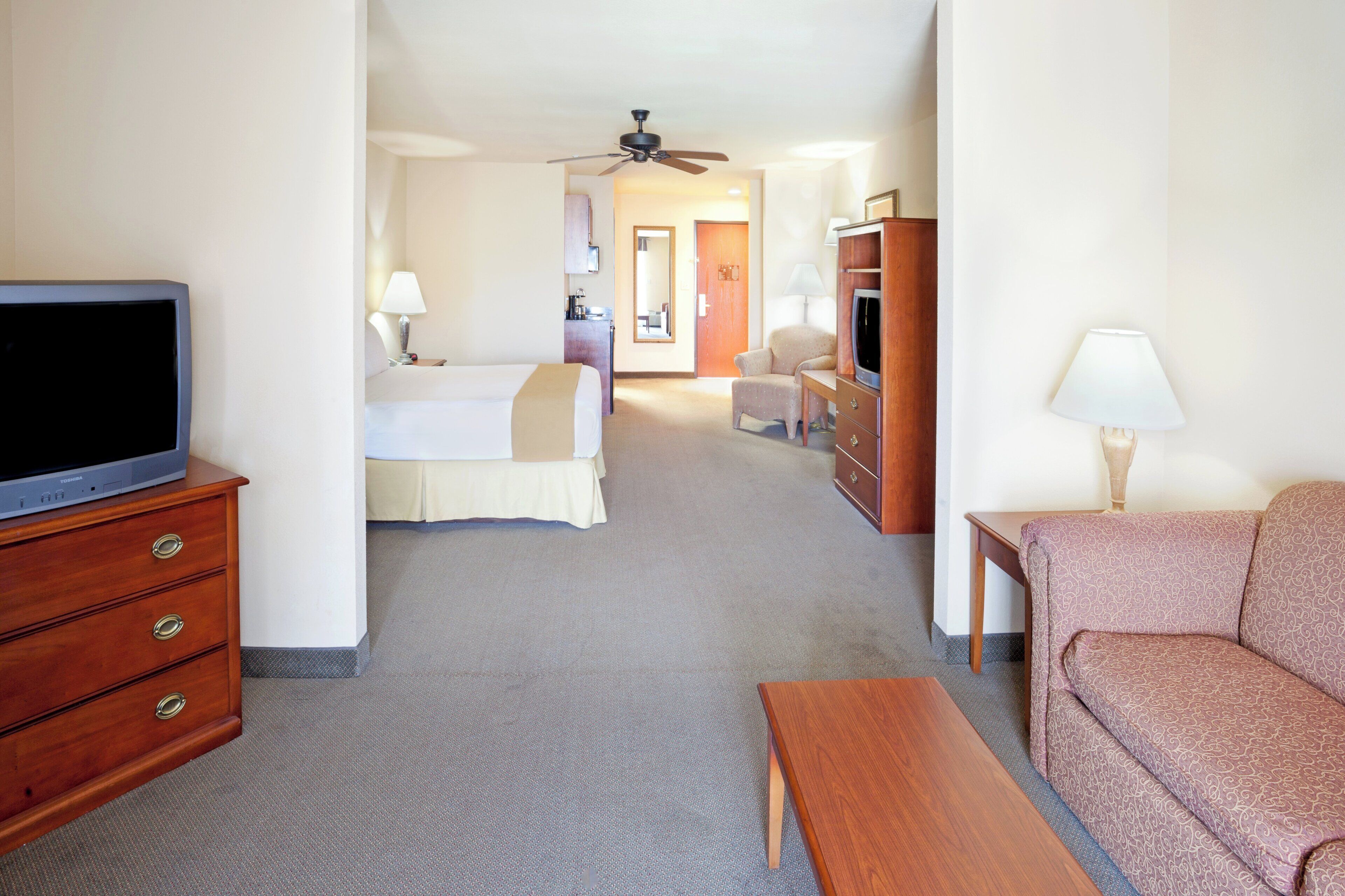 A hotel room with a television, a sofa, a desk, a chair, a bed, and a bathroom visible in the background.