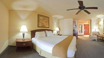 A hotel room with a large bed, two bedside tables with lamps, a ceiling fan, and a door leading to a bathroom.